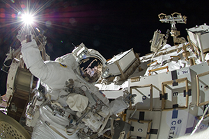 Image of an astronaut on a space walk performaing maintenance activities to a vehicle.